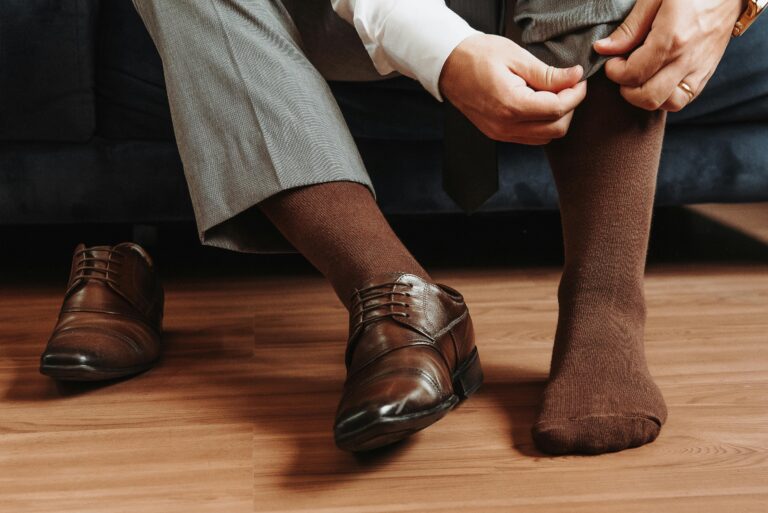 Man adjusting brown socks with leather shoes on wooden floor, elegant style.