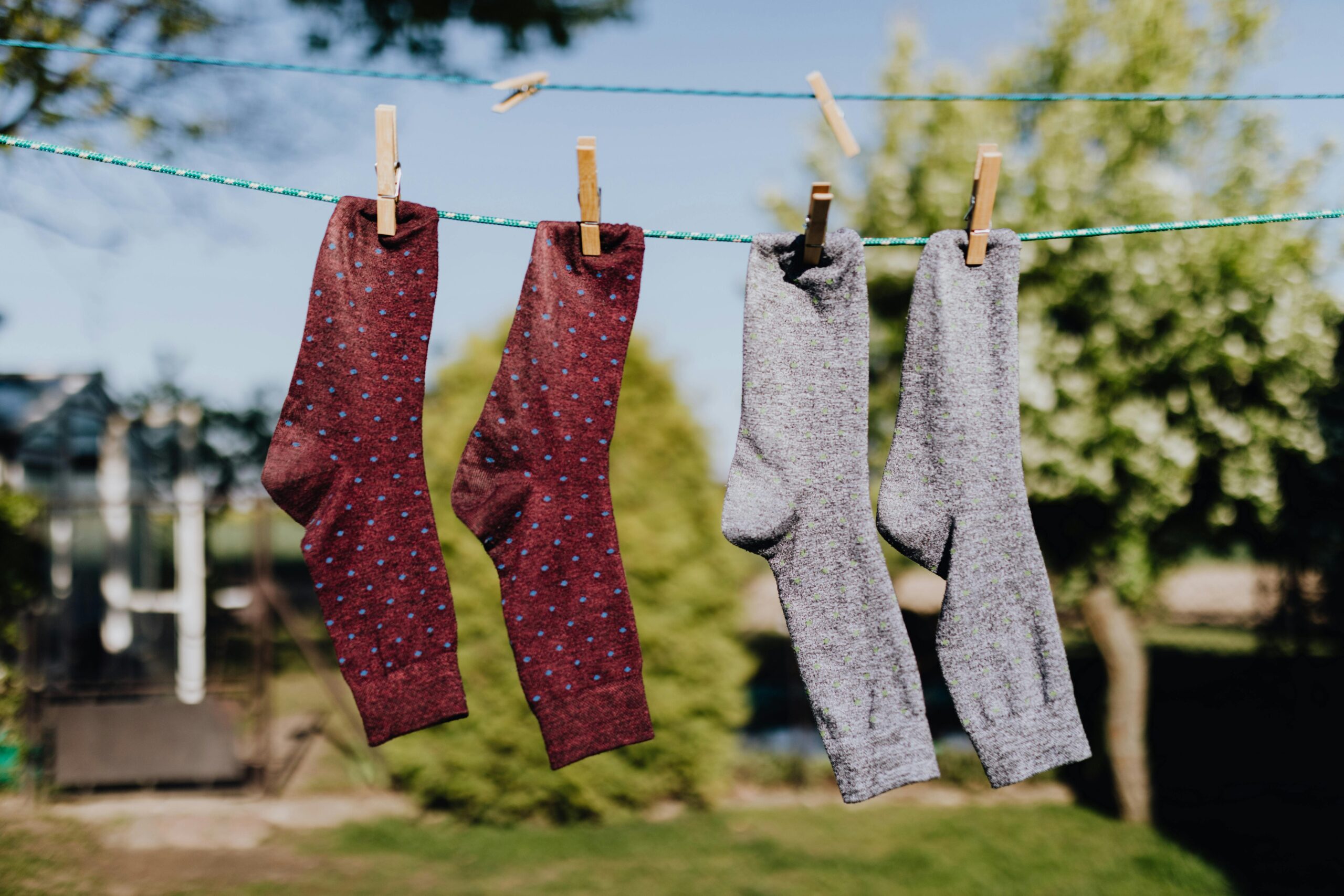 Soft focus of washed multicolored socks hanging on rope with clothespins outdoors on sunny summer day against natural background